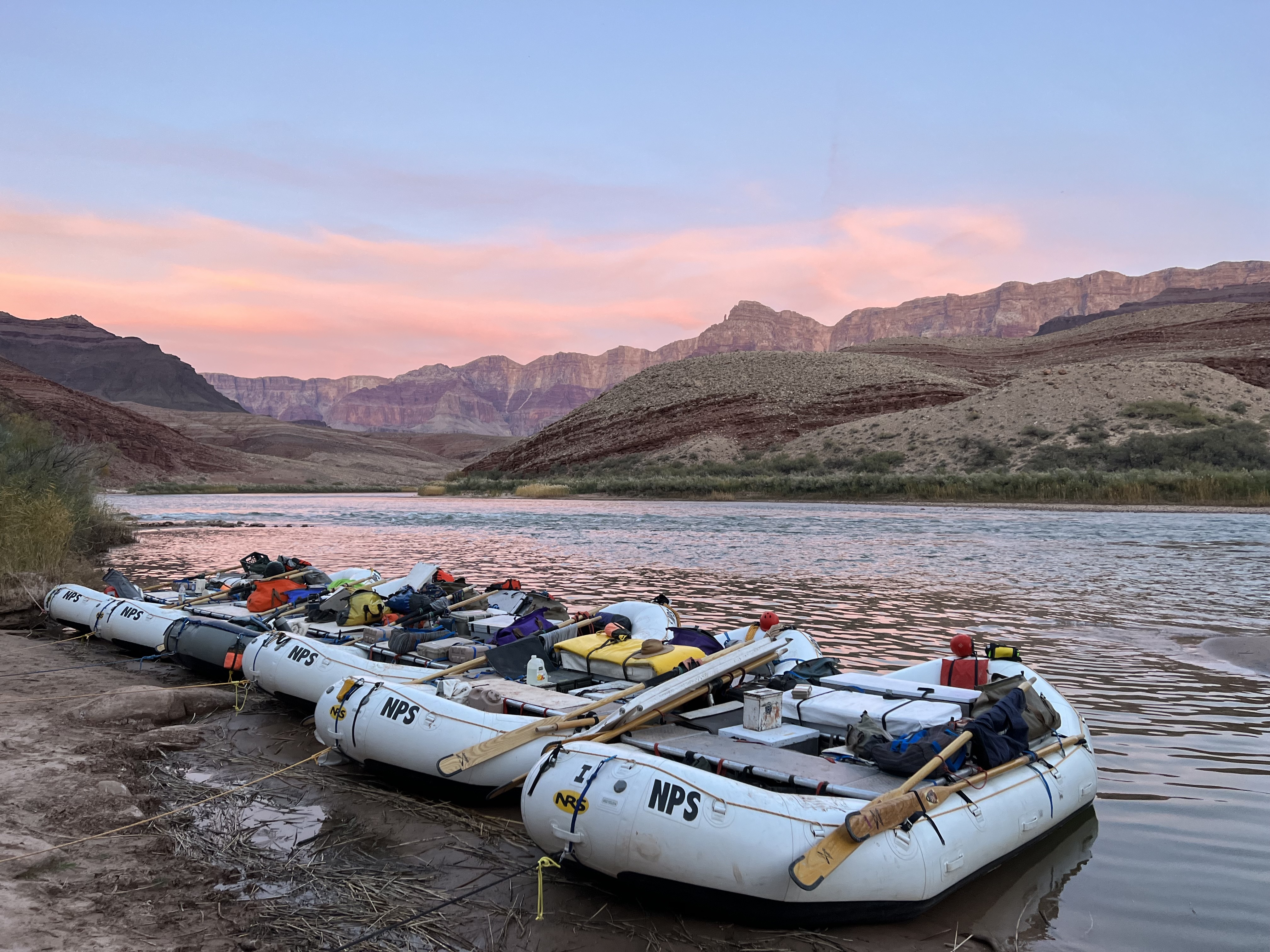 Sunset from Unkar Delta along the Colorado River on Rafting Trip. Pink skies in the background and boats in the foreground.