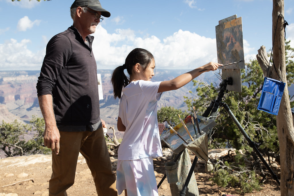 An artist lets a girl paint with him on the rim of Grand Canyon