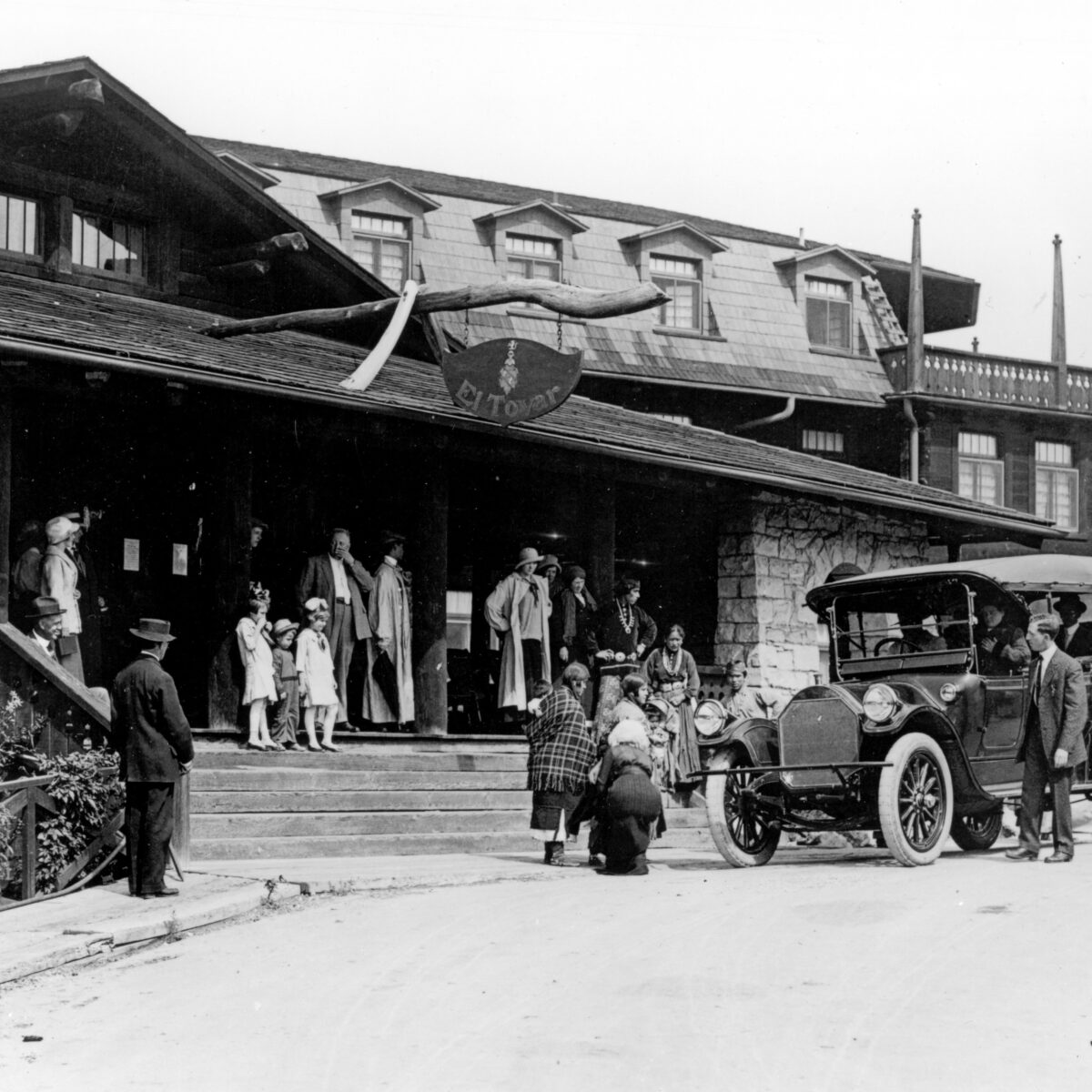 VISITORS STANDING AROUND THE FRONT ENTRANCE  TO THE EL TOVAR HOTEL. HOPI DEMONSTRATORS POSING. TOUR AUTOMOBILE. CIRCA 1922. FRED HARVEY PHOTO.