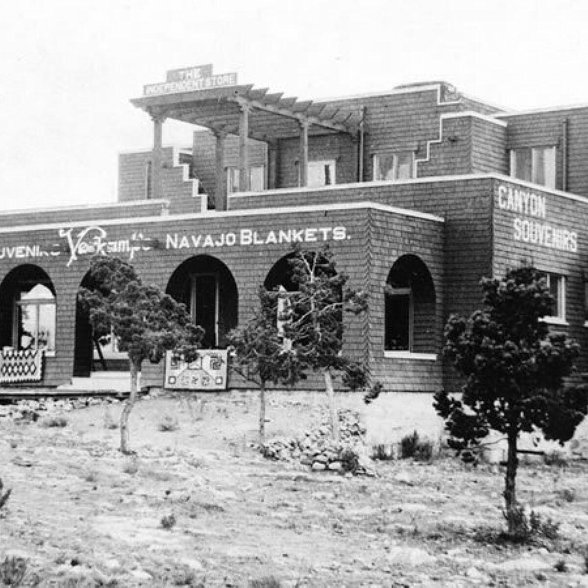 Black and white photo of Verkamps store with rugs outside Signs read Canyon souvenirs Navajo blankets Circa 1910, Photo from Grand Canyon Archives, GRCA, 11365