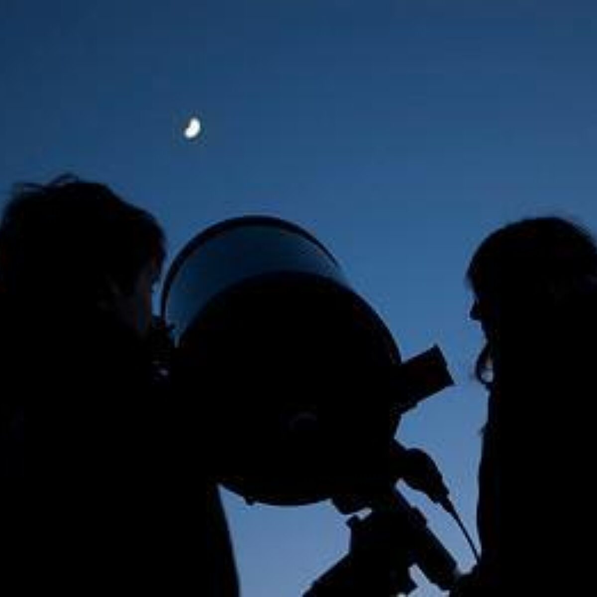 Two people are silhoutted in the night sky with a telescope