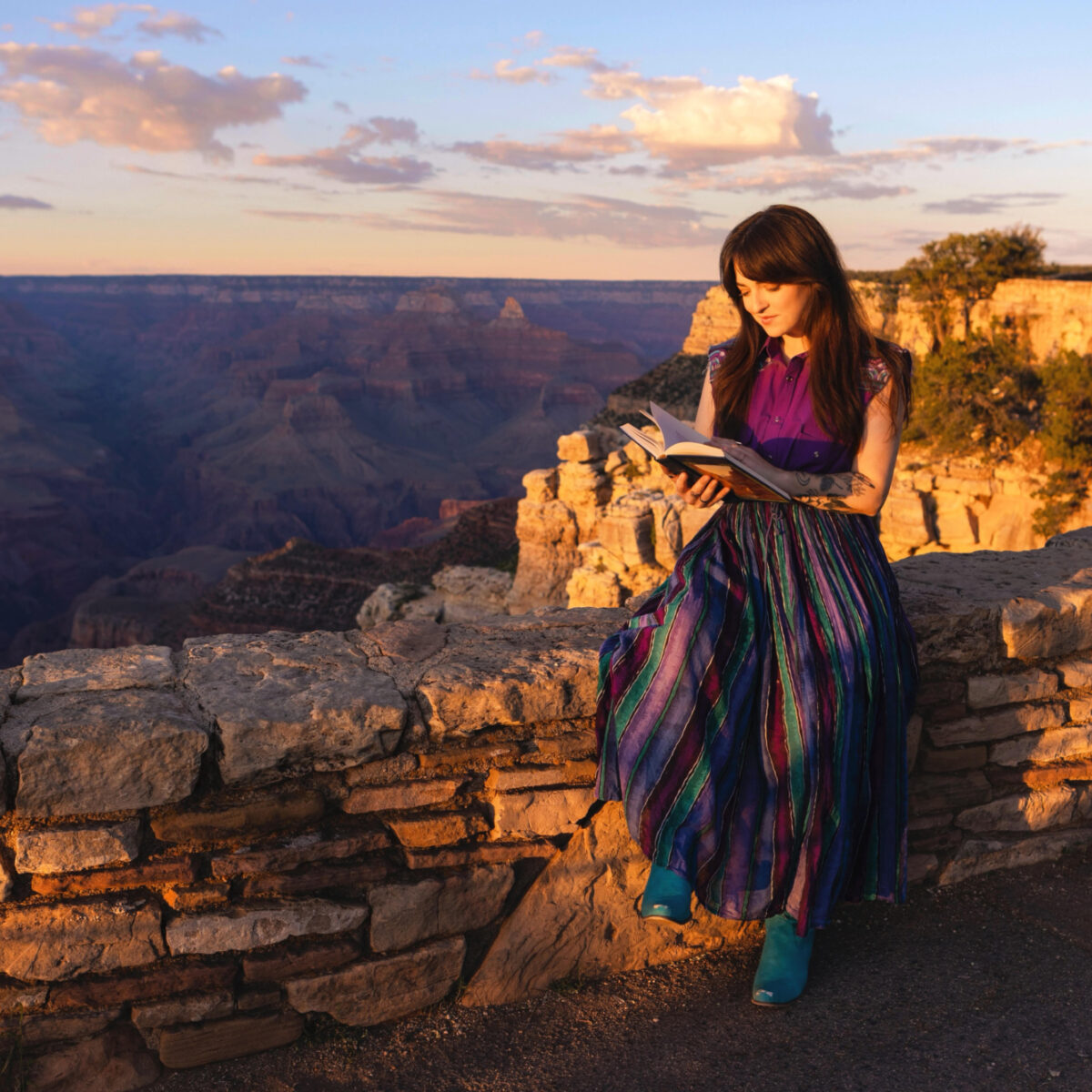Woman sitting on the South Rim of Grand Canyon reading from a book.