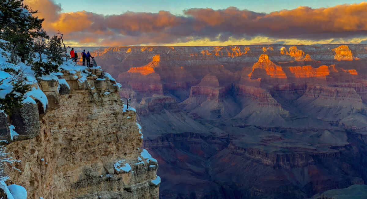 Sunset red and blue colors over Grand Canyon with hikers standing on peak watching clouds in the distance, NPS photo
