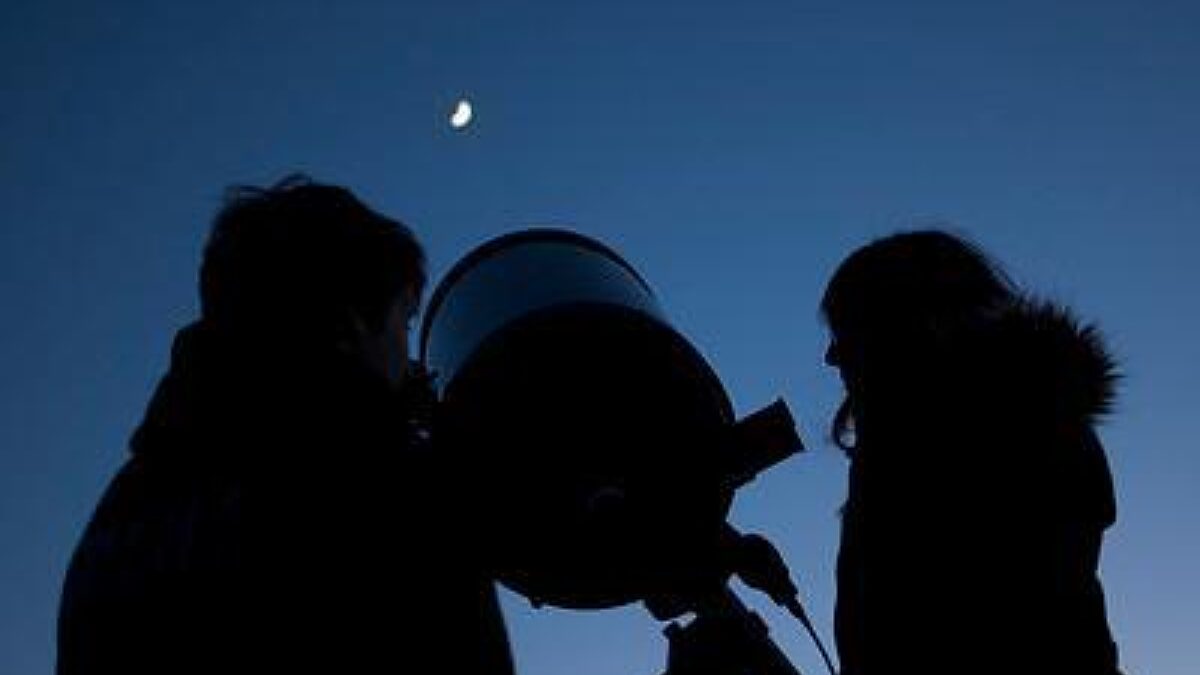 Two people are silhoutted in the night sky with a telescope