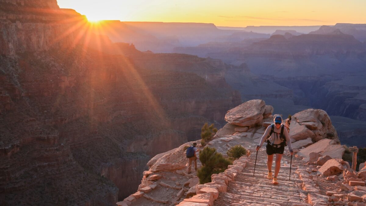 A hiker walks up the trail on the South Kaibab Trail with sunset colors behind her