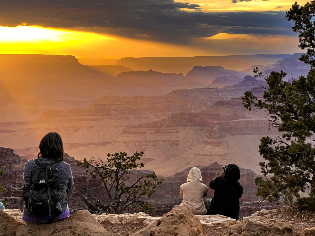 Three people watch the sunset at Yavapai Point