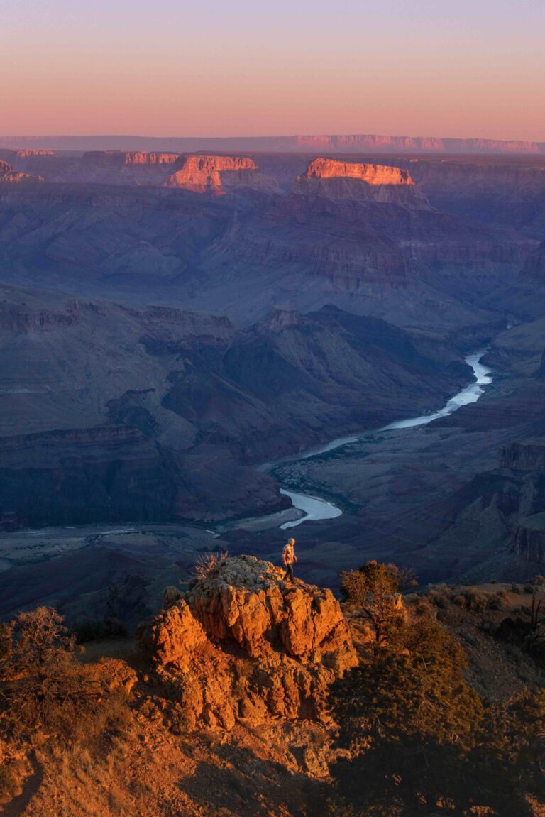 Small hiker standing on rock in front of canyon overlook at sunset copy