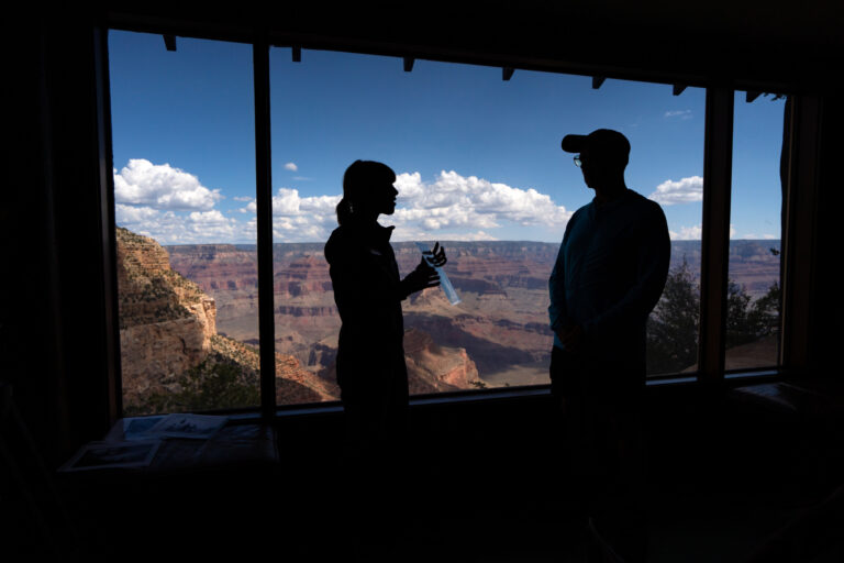Two silhouetted figures standing talking in front of open window PC David Wallace