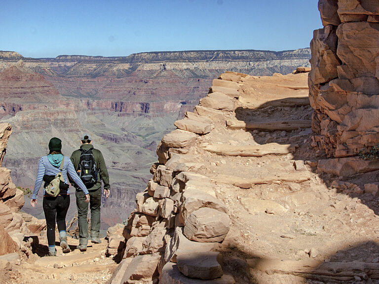 2 day hikers descending have just turned the corner of a rugged backcountry trail switchback built into a cliff. NPS/M.Quinn