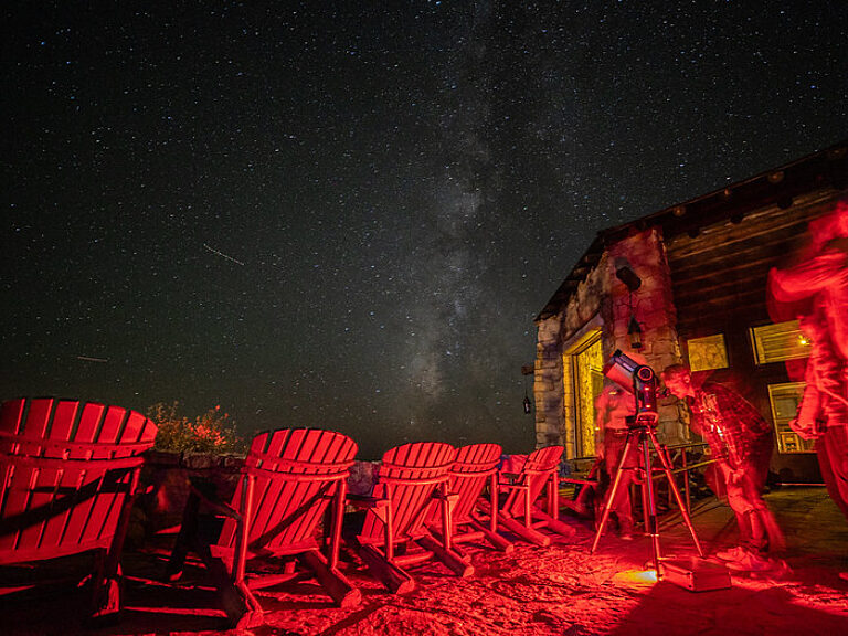Milky Way over Grand Canyon with visitors looking through telescopes on the North Rim with red lights illuminated.