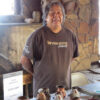 Carlos Laate standing in front of clay pottery artwork at table