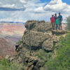Family of 4 standing and smiling for photo on rock edge at Grand Canyon