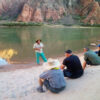Field Institute guide educating group of hiker tourists seated on beach with water and canyon in background