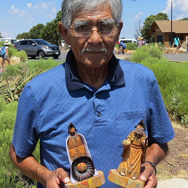 Coolidge Roy Jr standing holding two wooden carvings