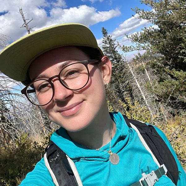 A woman wearing a light green hat and a blue sun hoodie with glasses on takes a selfie