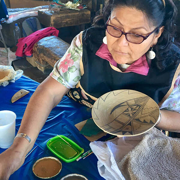Evvy Trujillo reaching across table working on painting pottery