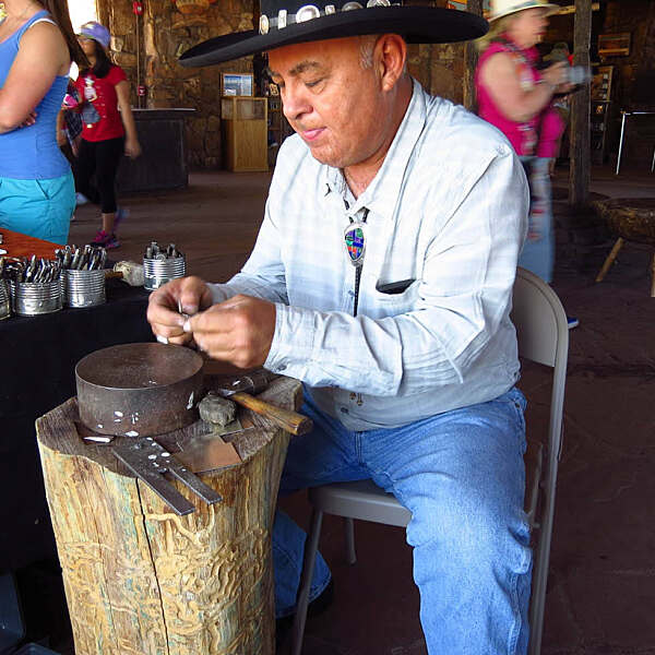 Patrick Yellowhorse working on jewelry piece on wood stump